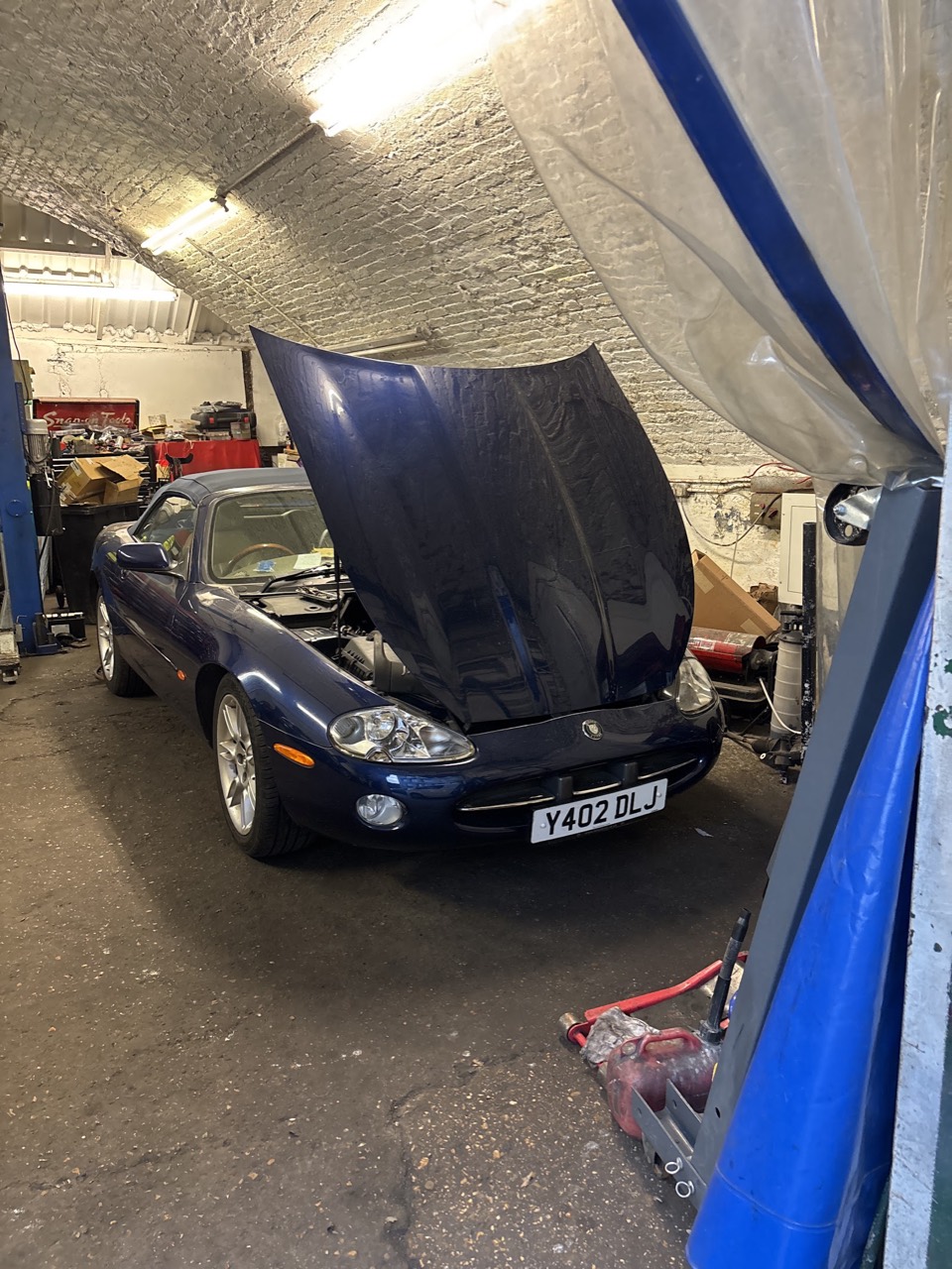 A dark blue Jaguar with its bonnet up inside the railway-arch workshop at Samet Auto Electrics in Lower Clapton.