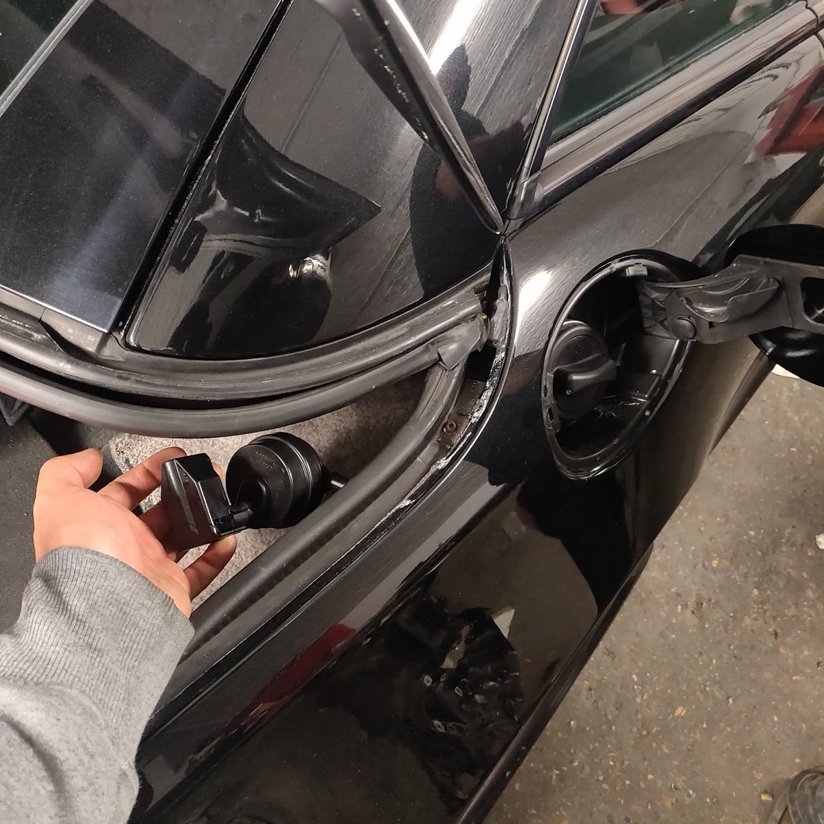 A hand holding a small electronic sensor removed from a black car during electrical repair at Samet Auto Electrics.